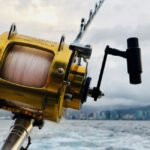 Angler on a boat in the deep blue ocean, battling a large game fish on the line with water splashing, showcasing the thril...